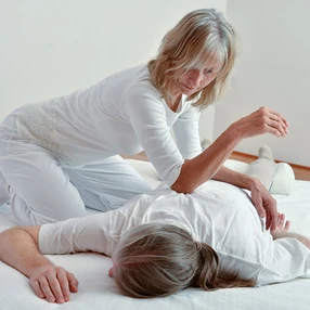 Shiatsu-Behandlung in Bauchlage, Behandlung mit Ellbogendruck entlang des Blasenmeridians direkt neben der Wirbelsäule. Durch diese Punkte werden alle Meridiane und damit der gesamte Körper zusätzlich gehandelt.